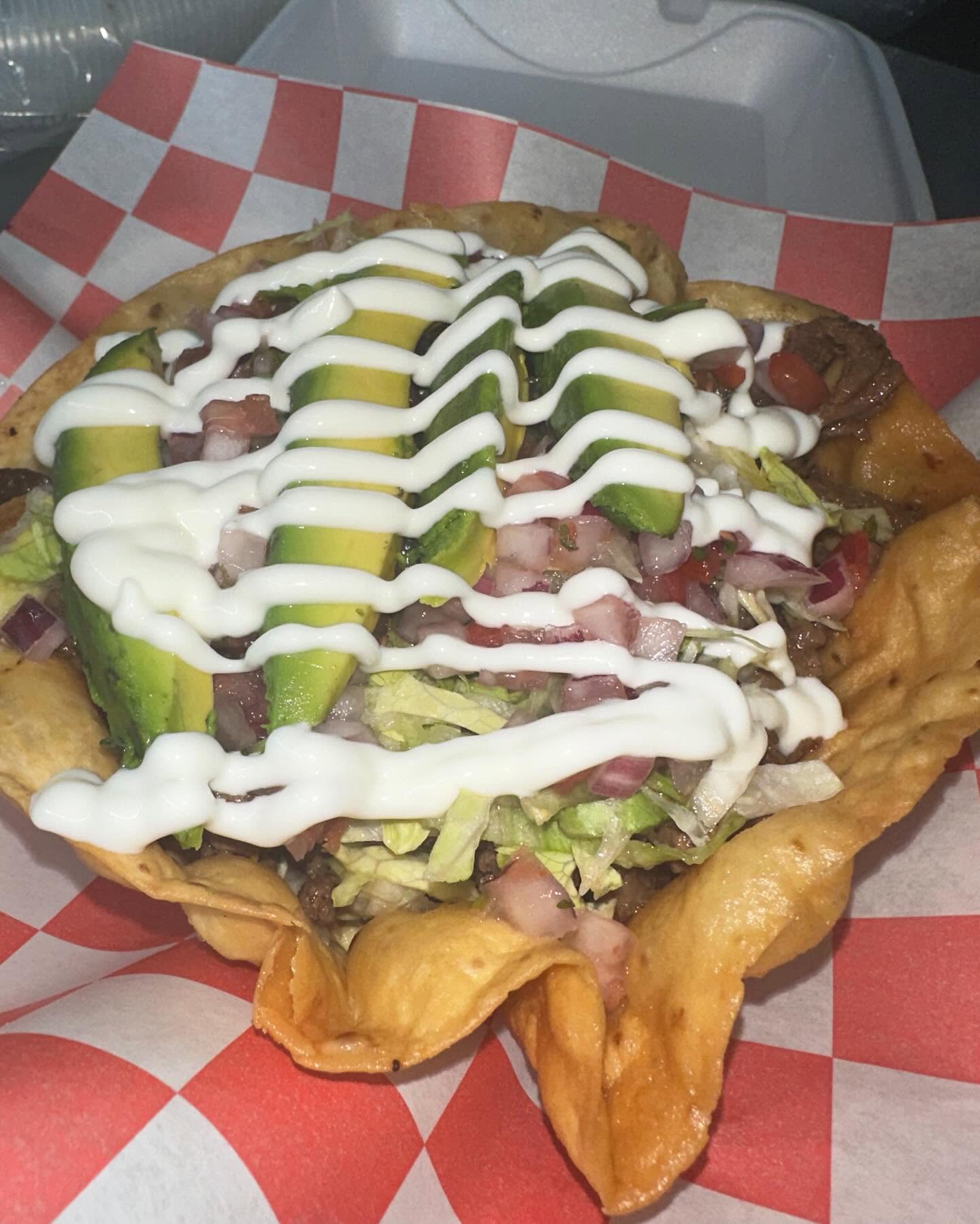 A loaded fried tostada bowl with avocado, crema, and pico de gallo